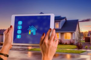 A person holding a tablet in front of house depicting a smart house .Key Partners Property Management can provide property management for properties like this.