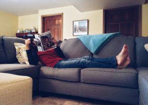 A person lying on a sofa reading newspaper
